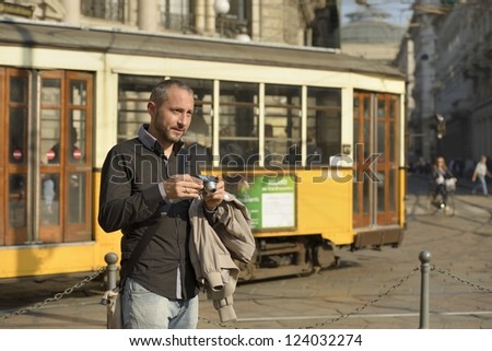 tourist photographing at Cordusio, Milan  portrait of  tourist man taking photos at square in city center, shot in bright light with a tram passing behind him