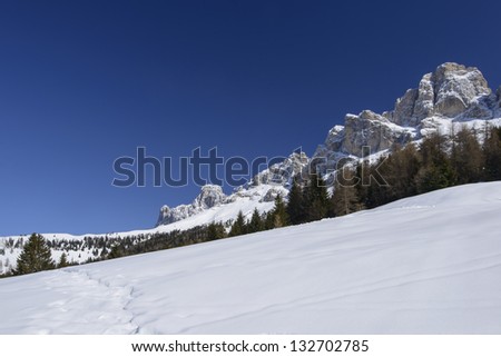 snowy slope and Rosengarten, Costalunga pass; bright snow over slope in Dolomites under famous mountain range, shot in bright light under deep blue sky