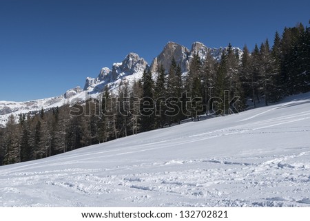 snowy meadows under Rotewand, Costalunga pass; bright snow over meadows on smooth slopes in Dolomites under famous mountain range, shot in bright light under deep blue sky