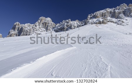 Rosengarten and empty Laurin ski run, Costalunga pass; steep ski run in Dolomites under rock cliffs of famous mountain range, shot in bright light under deep blue sky