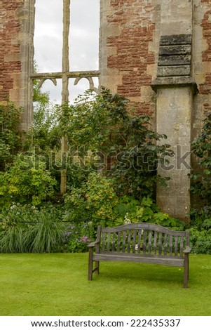 wooden bench in garden at Bishop palace ,Wells view of wooden bench near ruined facade with stone windows at garden of historic palace,  shot in bright light under a cloudy sky