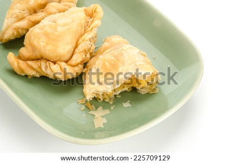 Image of curry puff with a bite taken out on green ceramic dish