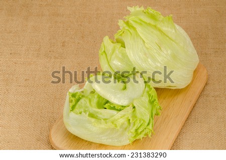 Image of green iceberg lettuce on wood cutting board on brown sack background