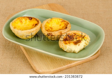 Image of egg tart with bite taken out in green ceramic dish on brown sack background