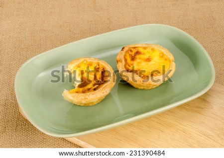 Image of egg tart with bite taken out in green ceramic dish on brown sack background