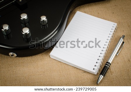Part of electric bass with blank paper and pen on brown sack background