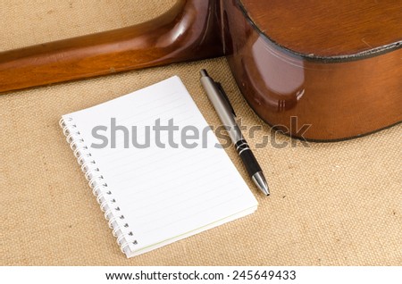 Image of white blank paper with pen on old acoustic guitar on brown sack background