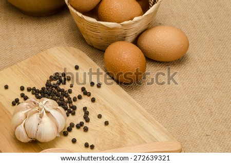 Wet eggs in bamboo woven bucket with garlic and black pepper on brown sack background
