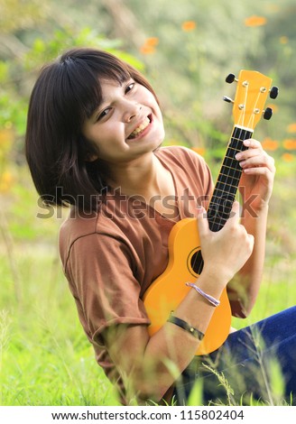 Young girl play guitar, look to the camera and smile in outdoor