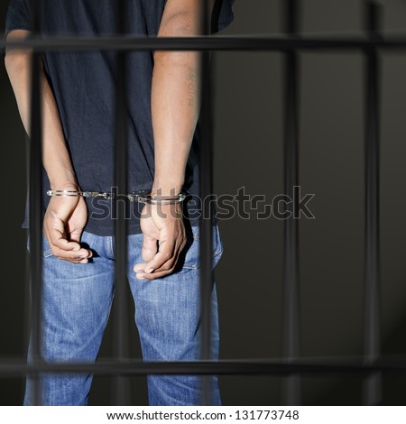 Prisoner locked in handcuffs in prison on black background