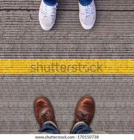 Two pairs of shoes standing on walkway with Yellow line separate