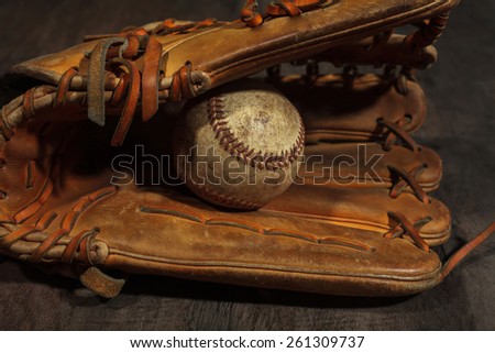Old baseball glove with weathered baseball on wood background