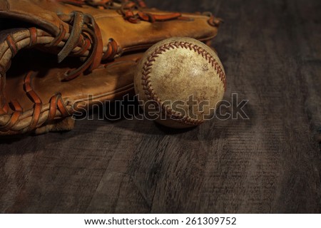 Old baseball glove with weathered baseball on wood background
