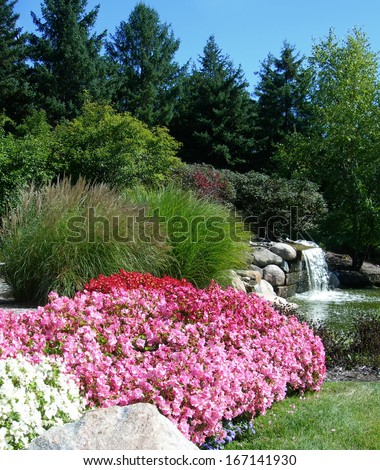 Landscape with pink flower beds tall decorative grass and waterfall