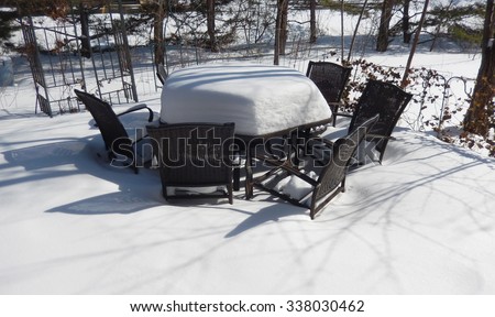 Backyard outdoor table and chairs on a patio covered with a thick layer of snow on a bright winter day