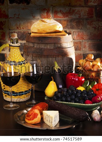Still life with wine and some fruits,vegetables, cheese and ham. Against the backdrop of a brick wall.
