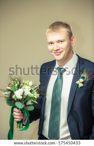 Groom is holding a flower\'s bouquet and smiling.