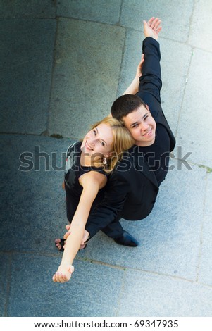 Boy and girl dressed in black looking up. Stand back to back outstretched hands.