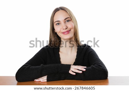 Happy smiling young woman with a straight long brown hair in a black sweater sits at a table having put hands