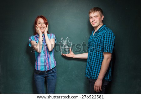 Man gives a gift to his girlfriend . Girl is delighted. Gift is drawn with chalk.