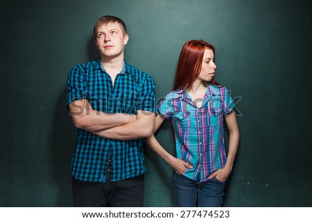Portrait Of Beautiful Young Couple Over Dark Green Wall. Hard times in relationships. Red-haired woman and blonde man in check shirts.