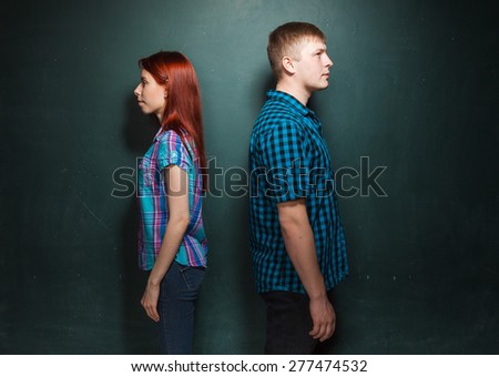 Beautiful Young Couple Over Dark Green Wall. They stand a back to each other. Quarrel, conflict. Hard time in relationships. Love story. Red-haired woman and blonde man in check shirts.