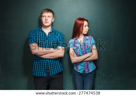 Portrait Of Beautiful Young Couple Over Dark Green Wall. Hard times in relationships. Red-haired woman and blonde man in check shirts.