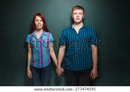 Beautiful Young Couple Over Dark Green Wall. Love story, acquaintance, flirtation. Red-haired woman and blonde man in check shirts.