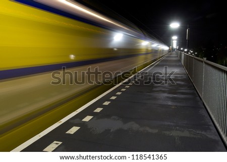 A yellow/blue colored train passing by a small railway station