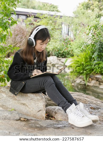 Young beautiful girl reading a book and  listen to music at the park