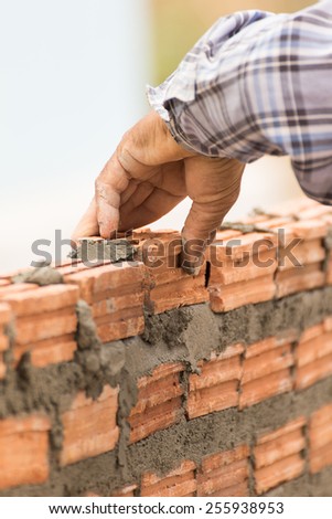 Bricklayer working in construction site of a brick wall. Bricklayer putting down another row of bricks in site