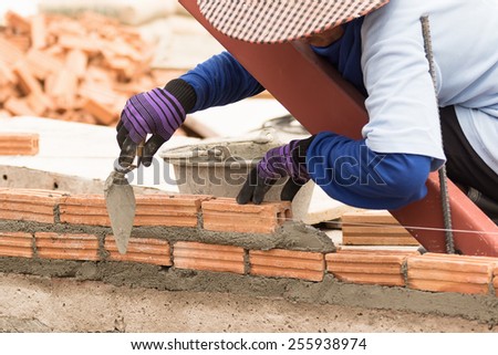 Bricklayer working in construction site of a brick wall. Bricklayer putting down another row of bricks in site