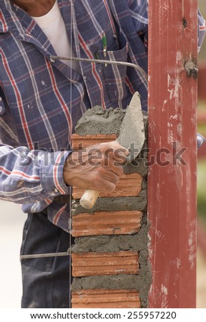 Bricklayer working in construction site of  brick wall. Bricklayer putting down another row of bricks in site