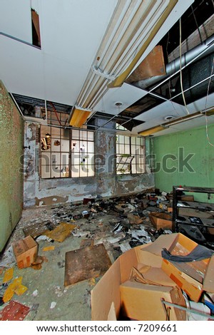 An abandoned office in a deserted industrial building. Paint peeling form the walls, frosted windows broken and in disrepair, & litter covering the floor