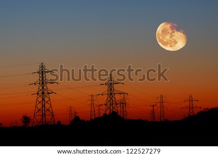 Energy Distribution Network - Electricity Pylons against Orange sky and Yellow Moon