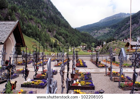 A small well-kept cemetery in the South Tyrolean mountains, colorful jewelry and iron grave crosses, forested mountains in the background A small cemetery in South Tyrol