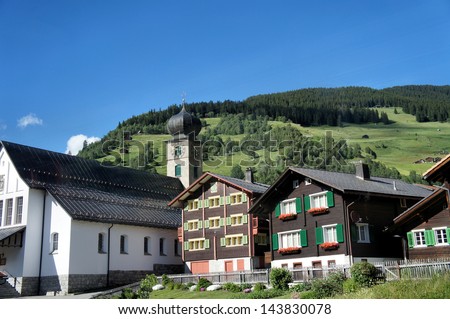 A mountain village in the canton of Graubunden, Switzerland, wooden houses with flower boxes, a steeple and blue sky/Mountain village in Switzerland