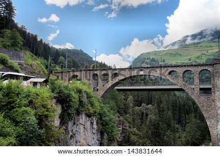View on a viaduct of the train and a road bridge in Graubunden in Switzerland; wooded ravine and blue sky with clouds/Swiss bridges