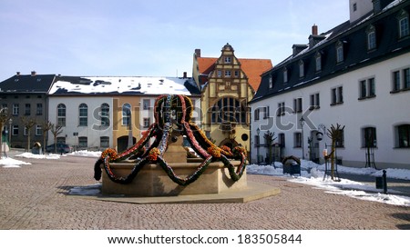 On the marketplace of the small town Auma in Thuringia is at Easter decorated the fountain with many colorful Easter eggs, in the background the town hall/ An Easter fountain in Thuringia, Germany