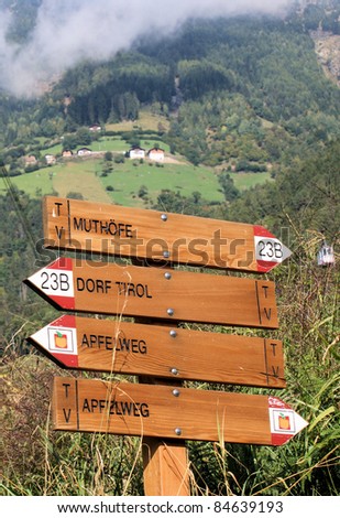 Hiking sign in South Tyrol; steep and forested slopes; clouds; farmhouses - called Muthöfe  Hiking sign in South Tyrol