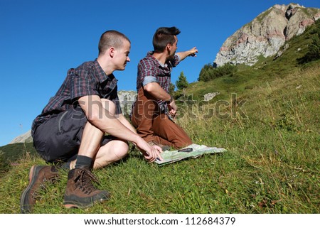 Two young backpackers reading a map and pointing on a mountain summit