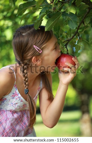 Little girl biting into an apple from an apple tree. Shallow depth of field.