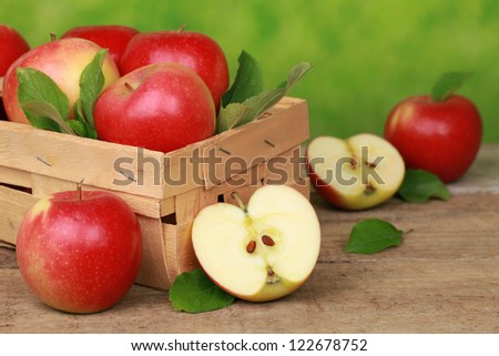 Apples with leaves in a wooden box on a table with green background