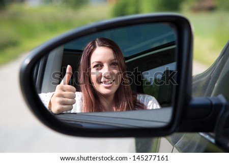 A happy driver leaning out of the window and showing thumbs up in the mirror
