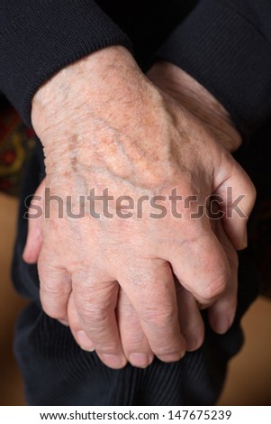 An old senior adult holds his hands crossed over his knee