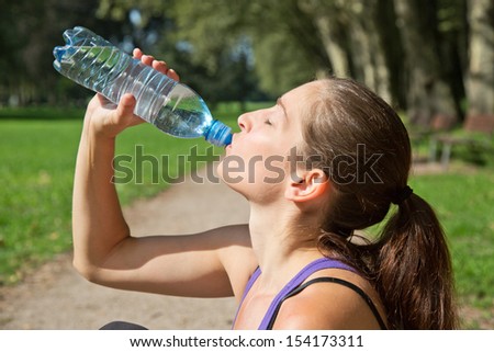 Attractive sporty woman drinking water from a bottle after jogging or running