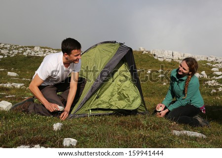 Two young people building up a tent in the mountains alps