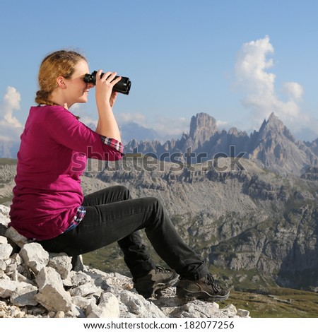 A young woman is watching the landscape in the mountains through binoculars