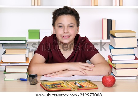Happy smiling boy doing homework at school in his exercise book