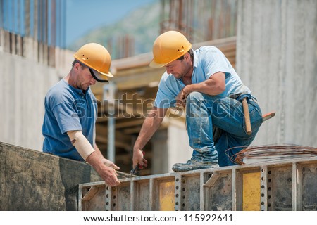 Two authentic construction workers collaborating in the installation of concrete formwork frames